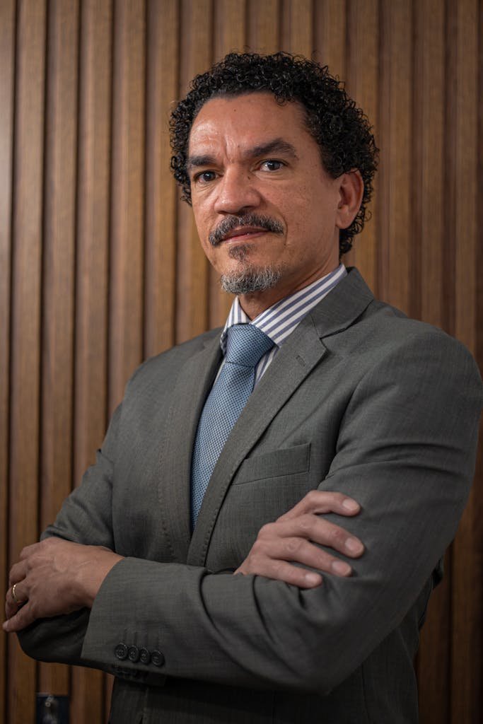 Confident businessman in a suit posing with arms crossed against wooden background.